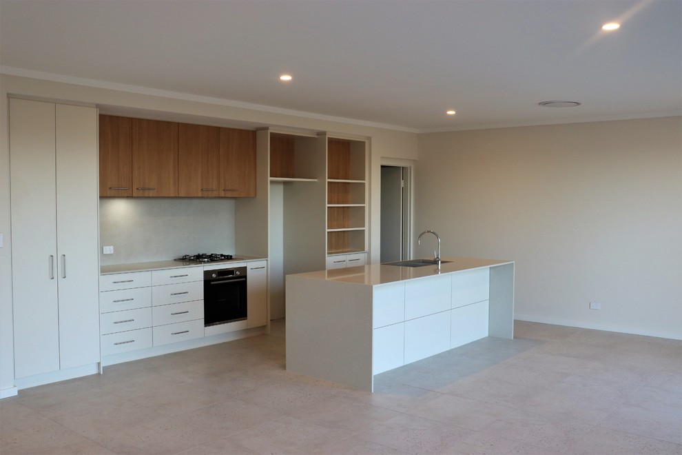This is an example of a large contemporary galley open plan kitchen in Perth with a drop-in sink, recessed-panel cabinets, medium wood cabinets, granite benchtops, beige splashback, ceramic splashback, black appliances, ceramic floors, with island, beige floor and white benchtop.
