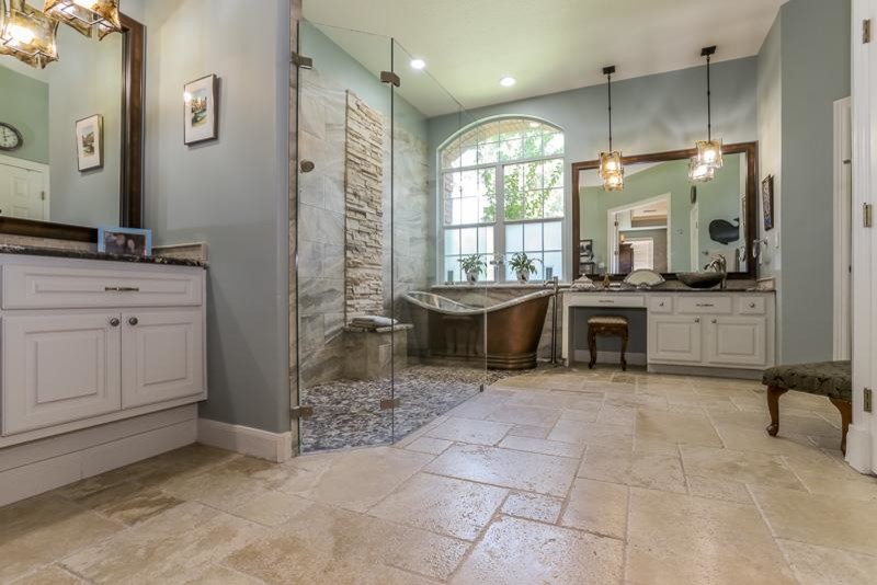 This is an example of a beach style master bathroom in Houston with a vessel sink, white cabinets, granite benchtops, a freestanding tub, a curbless shower, beige tile, blue walls, travertine floors and raised-panel cabinets.