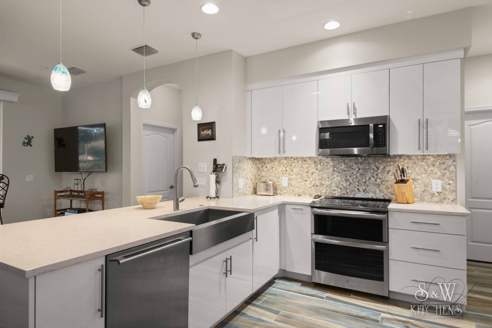 Small modern l-shaped open plan kitchen in Tampa with a farmhouse sink, flat-panel cabinets, white cabinets, quartz benchtops, multi-coloured splashback, glass tile splashback, stainless steel appliances, porcelain floors, a peninsula, blue floor and white benchtop.