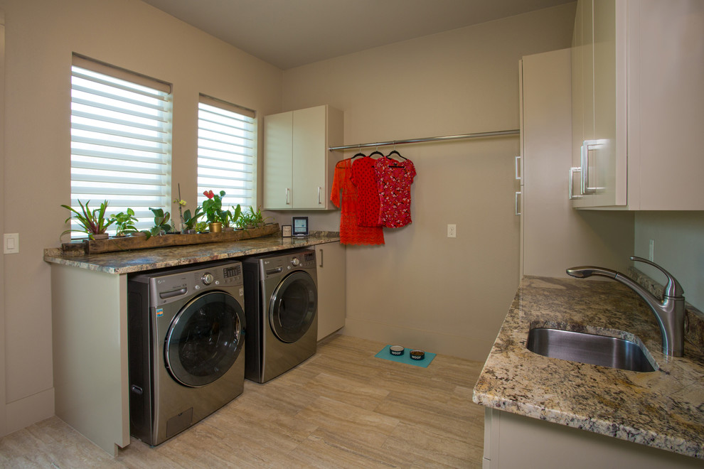 This is an example of a mid-sized mediterranean galley dedicated laundry room in Austin with an undermount sink, flat-panel cabinets, beige cabinets, granite benchtops, beige walls, porcelain floors and a side-by-side washer and dryer.