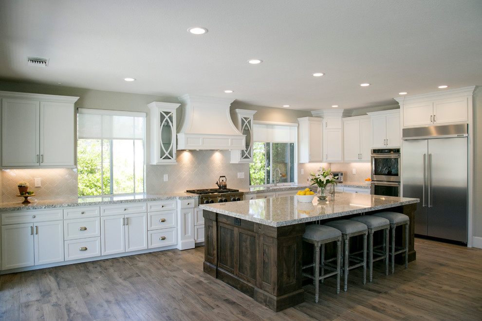 Photo of a large transitional l-shaped open plan kitchen in San Diego with an undermount sink, shaker cabinets, white cabinets, granite benchtops, white splashback, glass tile splashback, stainless steel appliances, light hardwood floors and with island.