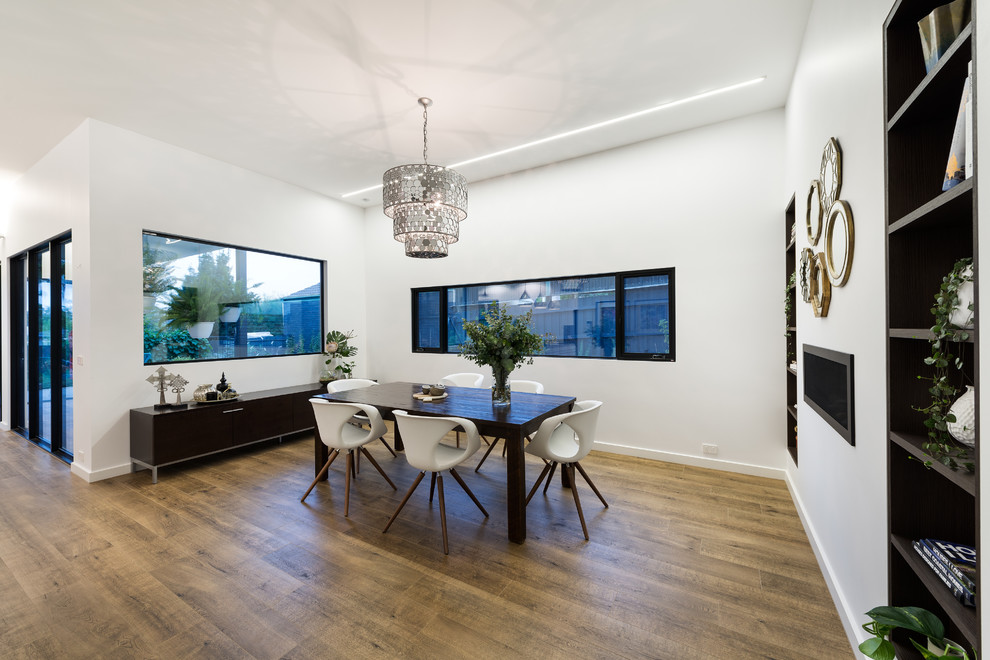 This is an example of a modern kitchen/dining combo in Melbourne with white walls, porcelain floors, a ribbon fireplace, a metal fireplace surround and brown floor.