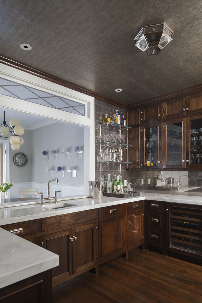 This is an example of a transitional u-shaped wet bar in Dallas with dark hardwood floors, an undermount sink, dark wood cabinets, white benchtop, beaded inset cabinets, marble benchtops, grey splashback, metal splashback and brown floor.
