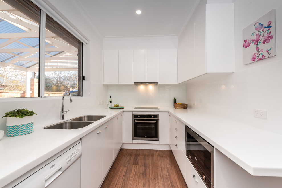 Inspiration for a small contemporary u-shaped separate kitchen in Other with a double-bowl sink, white cabinets, quartz benchtops, white splashback, medium hardwood floors, flat-panel cabinets and stainless steel appliances.