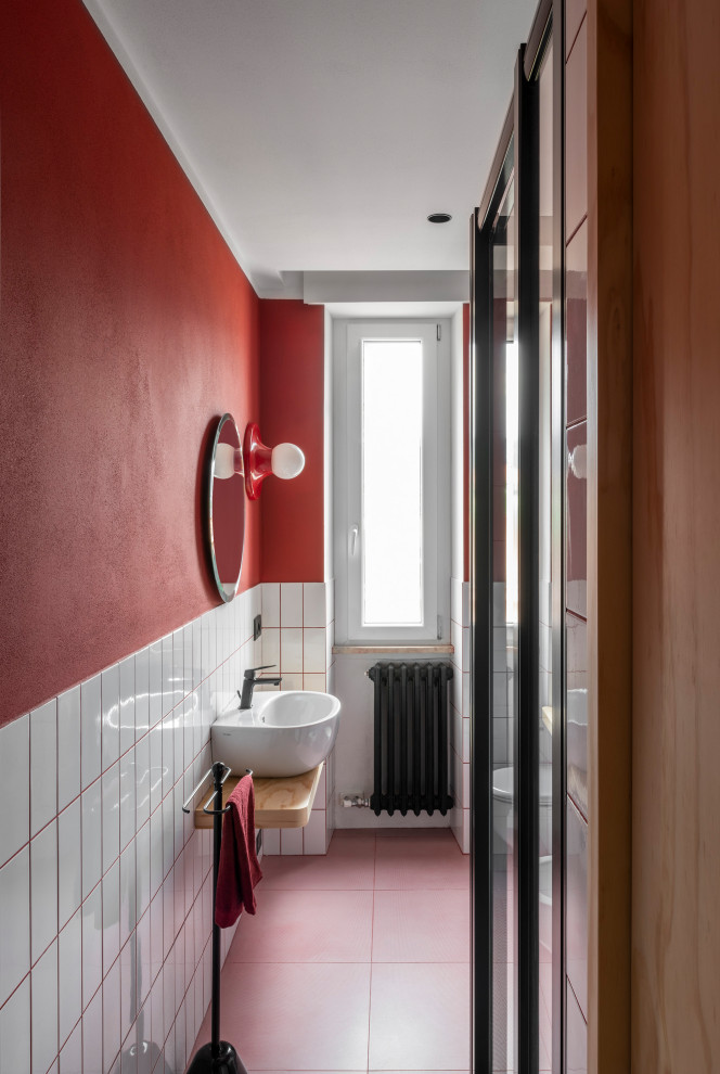 Mid-sized contemporary powder room in Venice with open cabinets, light wood cabinets, a two-piece toilet, white tile, ceramic tile, red walls, porcelain floors, a wall-mount sink, wood benchtops, pink floor and a floating vanity.