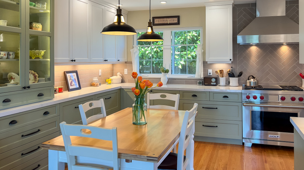 Foto på ett stort lantligt vit kök, med en rustik diskho, skåp i shakerstil, gröna skåp, bänkskiva i kvarts, grått stänkskydd, stänkskydd i porslinskakel, rostfria vitvaror och mellanmörkt trägolv