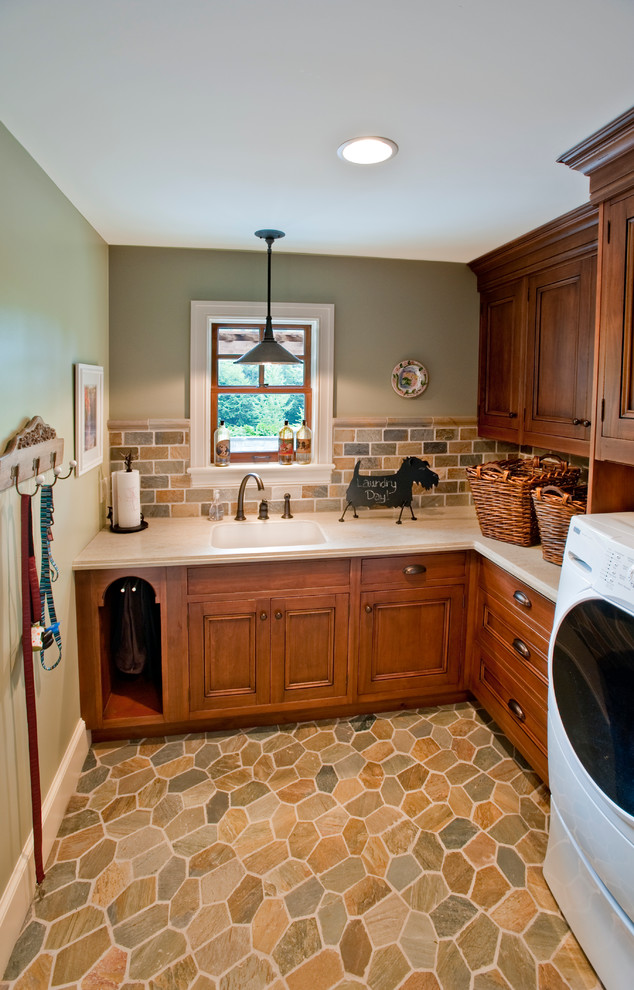 Photo of a mid-sized country l-shaped dedicated laundry room in Other with an integrated sink, medium wood cabinets, solid surface benchtops, grey walls, a side-by-side washer and dryer, travertine floors, beige floor and recessed-panel cabinets.