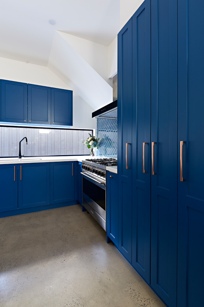 Photo of a mid-sized transitional l-shaped kitchen pantry in Melbourne with a double-bowl sink, shaker cabinets, blue cabinets, blue splashback, ceramic splashback, stainless steel appliances, concrete floors, with island, grey floor, white benchtop and quartz benchtops.