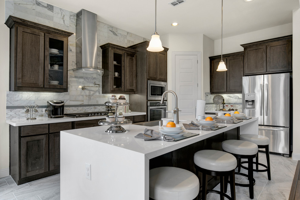 Design ideas for a large transitional l-shaped eat-in kitchen in Dallas with a farmhouse sink, recessed-panel cabinets, dark wood cabinets, quartzite benchtops, grey splashback, stone tile splashback, stainless steel appliances, ceramic floors, with island and grey floor.