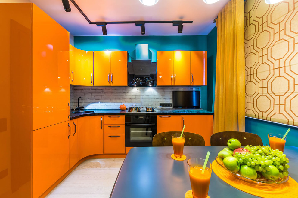 Photo of a mid-sized contemporary l-shaped eat-in kitchen in Other with flat-panel cabinets, orange cabinets, laminate benchtops, black appliances, laminate floors, no island, beige floor, a drop-in sink, white splashback and brick splashback.