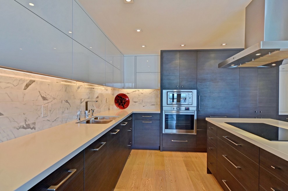Large minimalist l-shaped light wood floor open concept kitchen photo in Toronto with a double-bowl sink, flat-panel cabinets, black cabinets, quartz countertops, white backsplash, stone tile backsplash, paneled appliances and an island