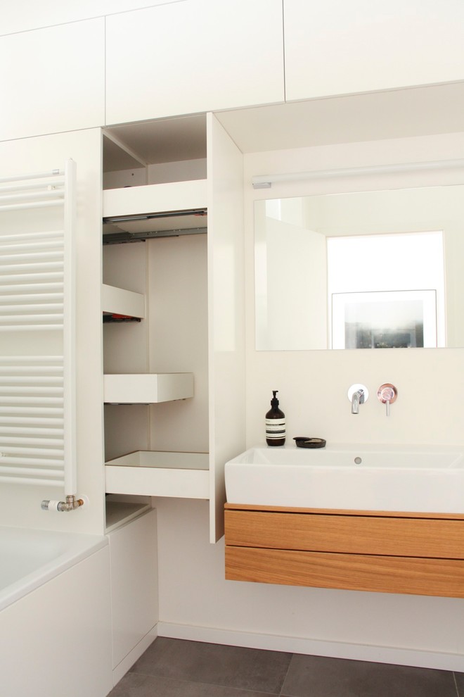 Inspiration for a mid-sized modern 3/4 bathroom in Berlin with flat-panel cabinets, light wood cabinets, an alcove tub, a shower/bathtub combo, a two-piece toilet, white tile, white walls, light hardwood floors, a vessel sink, wood benchtops, an open shower and white benchtops.