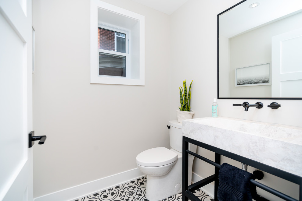 This is an example of a small contemporary powder room in Montreal with black cabinets, a one-piece toilet, multi-coloured tile, beige walls, ceramic floors, an integrated sink, marble benchtops, multi-coloured floor, grey benchtops and a freestanding vanity.