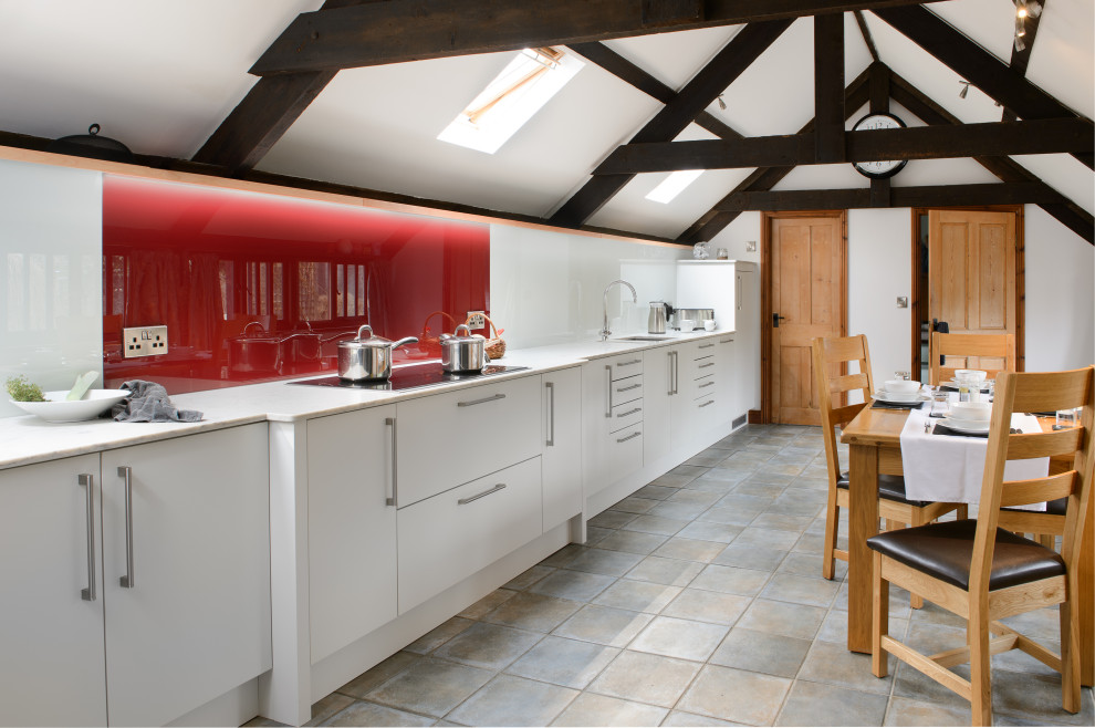 コーンウォールにある高級な広いコンテンポラリースタイルのおしゃれなキッチン (ダブルシンク、フラットパネル扉のキャビネット、白いキャビネット、オニキスカウンター、赤いキッチンパネル、ガラス板のキッチンパネル、黒い調理設備、セメントタイルの床、アイランドなし、ベージュの床、白いキッチンカウンター、表し梁) の写真