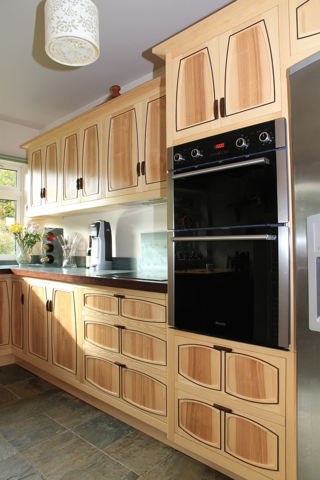 Design ideas for a mid-sized arts and crafts l-shaped separate kitchen in Other with a single-bowl sink, flat-panel cabinets, light wood cabinets, green splashback, stone slab splashback, black appliances, slate floors and no island.