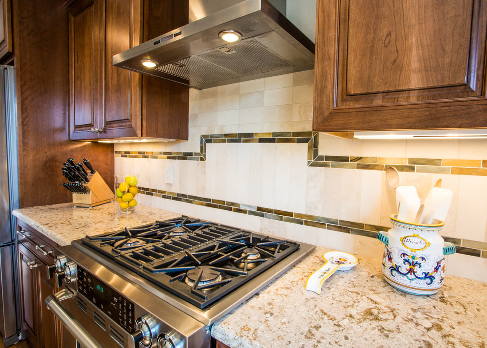 Inspiration for a large transitional l-shaped medium tone wood floor and brown floor eat-in kitchen remodel in Denver with a farmhouse sink, raised-panel cabinets, medium tone wood cabinets, granite countertops, beige backsplash, stone tile backsplash, stainless steel appliances and an island