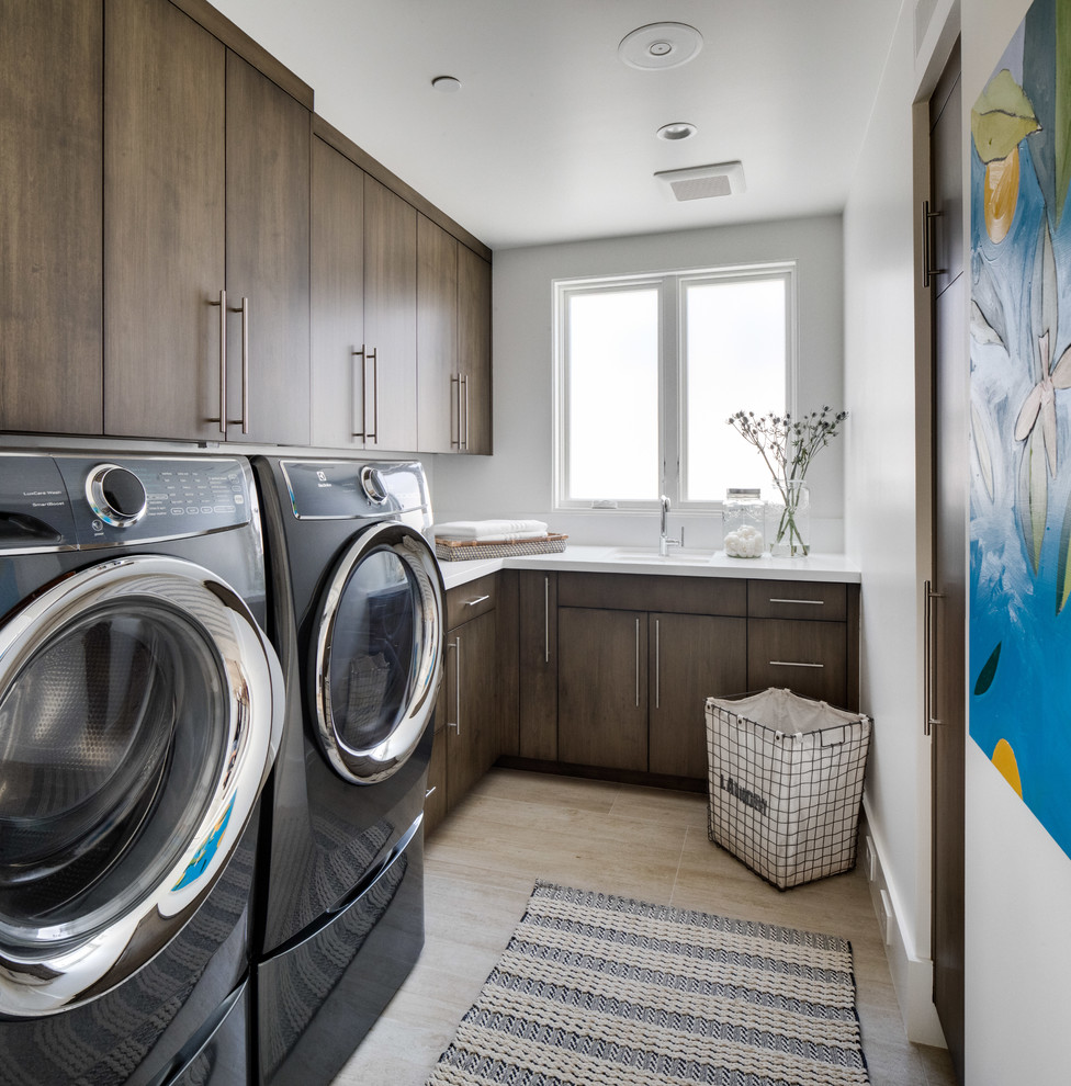 Contemporary l-shaped dedicated laundry room in Los Angeles with a single-bowl sink, flat-panel cabinets, dark wood cabinets, white walls, a side-by-side washer and dryer, beige floor and white benchtop.