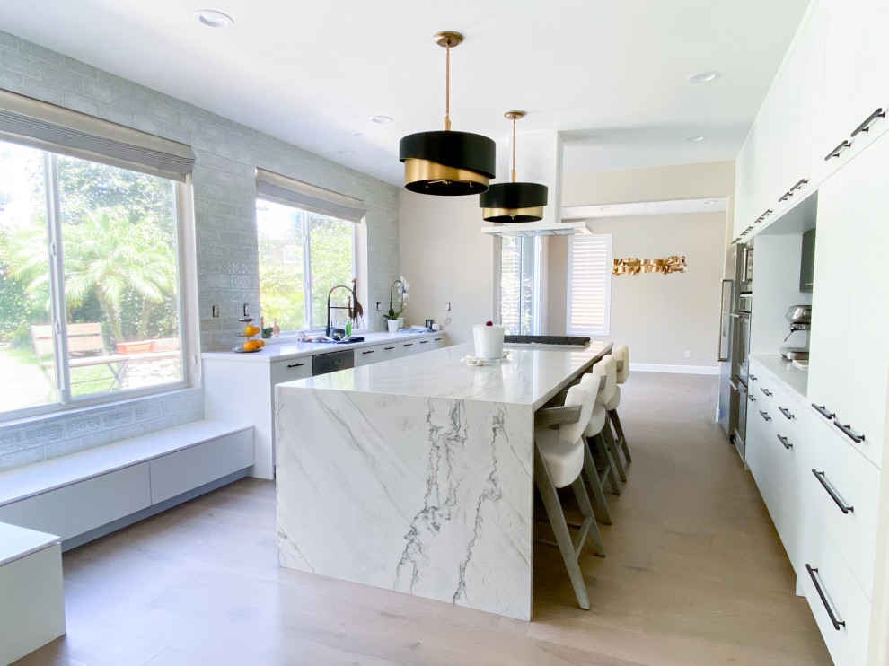 Photo of a large modern u-shaped kitchen in Orange County with flat-panel cabinets, white cabinets, quartz benchtops, ceramic splashback, stainless steel appliances, vinyl floors, with island and beige benchtop.