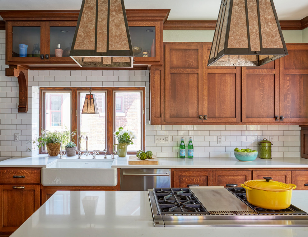 Inspiration for a mid-sized arts and crafts kitchen in Milwaukee with a farmhouse sink, shaker cabinets, medium wood cabinets, quartz benchtops, white splashback, subway tile splashback, stainless steel appliances, medium hardwood floors, with island, brown floor and white benchtop.