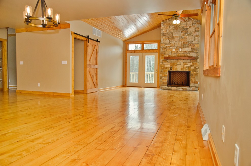 Inspiration for a large rustic open concept light wood floor and brown floor home design remodel with beige walls, a wood stove and a stone fireplace