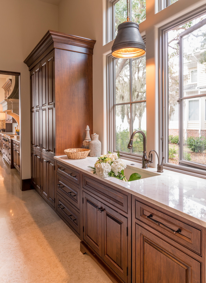 Photo of a large mediterranean l-shaped eat-in kitchen in Atlanta with a farmhouse sink, raised-panel cabinets, medium wood cabinets, white splashback, stone slab splashback, panelled appliances, limestone floors and with island.