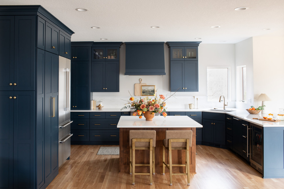 Example of a large transitional light wood floor kitchen design with an undermount sink, shaker cabinets, blue cabinets, quartz countertops, white backsplash, quartz backsplash, stainless steel appliances, an island and white countertops