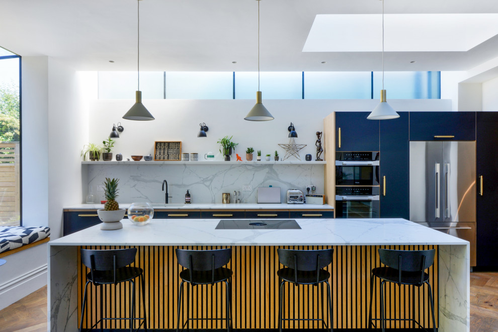 Modern inredning av ett flerfärgad flerfärgat kök, med en undermonterad diskho, släta luckor, blå skåp, marmorbänkskiva, flerfärgad stänkskydd, stänkskydd i marmor, rostfria vitvaror, mellanmörkt trägolv, en köksö och brunt golv