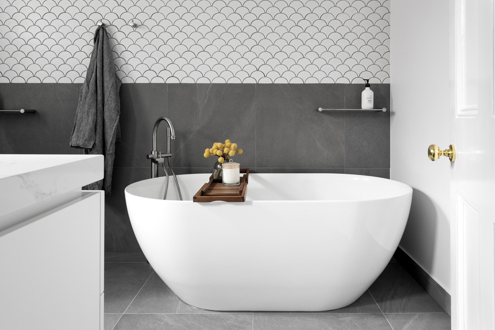 This is an example of a contemporary bathroom in Melbourne with white cabinets, a freestanding tub, gray tile, white tile, white walls, grey floor and white benchtops.