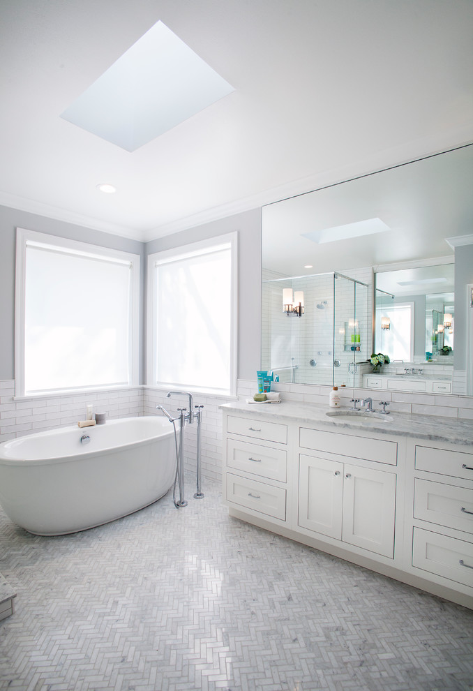 Photo of a large contemporary master bathroom in St Louis with beaded inset cabinets, white cabinets, a freestanding tub, a corner shower, a two-piece toilet, gray tile, subway tile, grey walls, marble floors, an undermount sink, marble benchtops, grey floor and grey benchtops.