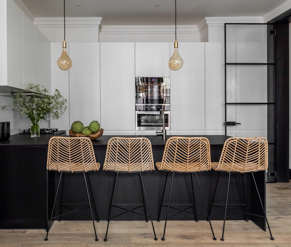Inspiration for a mid-sized contemporary u-shaped open plan kitchen in London with an integrated sink, black cabinets, white splashback, glass sheet splashback, stainless steel appliances, light hardwood floors, with island, brown floor, black benchtop and flat-panel cabinets.