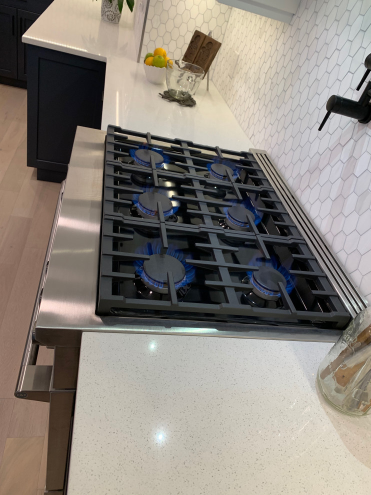 Example of a large transitional light wood floor and coffered ceiling kitchen design with an undermount sink, shaker cabinets, white cabinets, quartzite countertops, stainless steel appliances, an island and white countertops