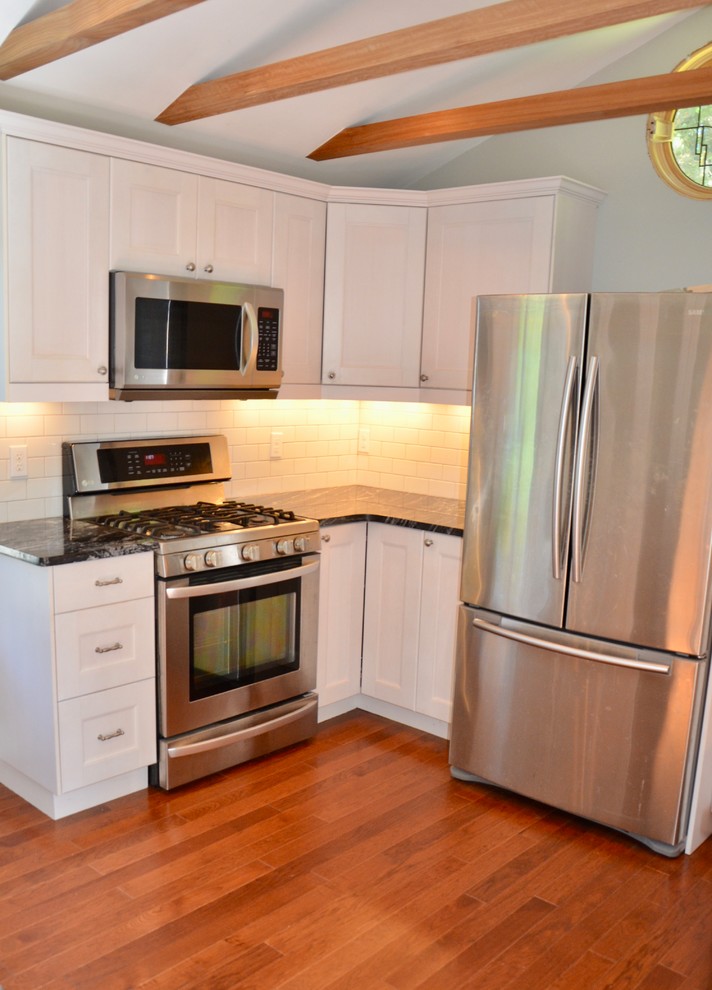 Example of a small transitional medium tone wood floor enclosed kitchen design with an undermount sink, glass-front cabinets, granite countertops, white backsplash, ceramic backsplash and stainless steel appliances
