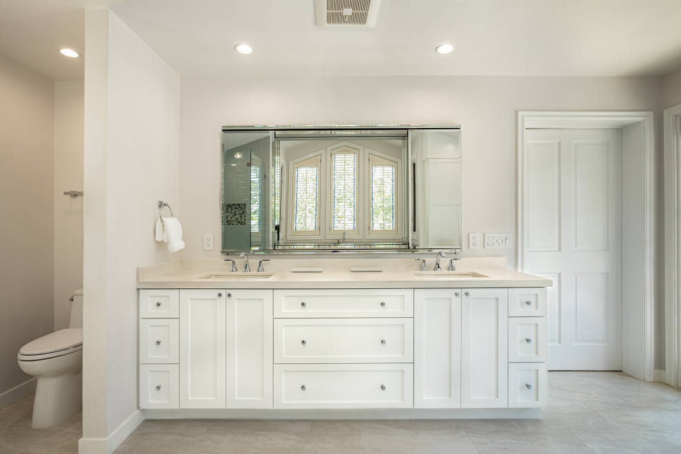 Large traditional master bathroom in Los Angeles with shaker cabinets, white cabinets, a freestanding tub, a corner shower, a one-piece toilet, gray tile, subway tile, white walls, porcelain floors, an undermount sink, engineered quartz benchtops, beige floor, a hinged shower door, white benchtops, a double vanity, a built-in vanity and vaulted.