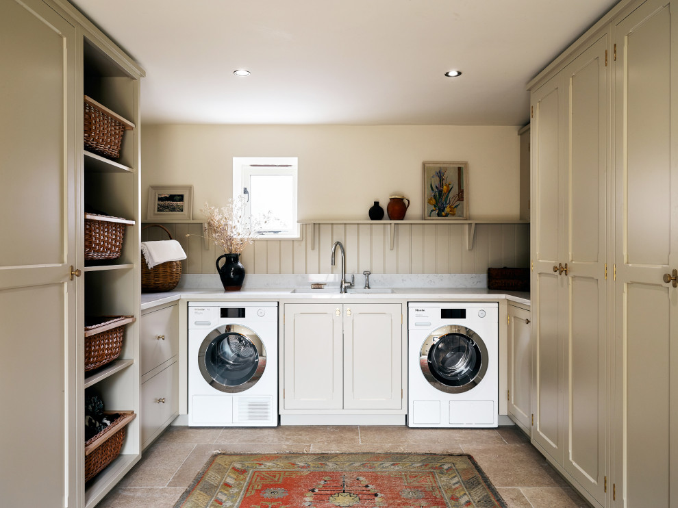 Design ideas for a country u-shaped laundry room in Other with an undermount sink, recessed-panel cabinets, beige cabinets, beige walls, a side-by-side washer and dryer, brown floor and white benchtop.