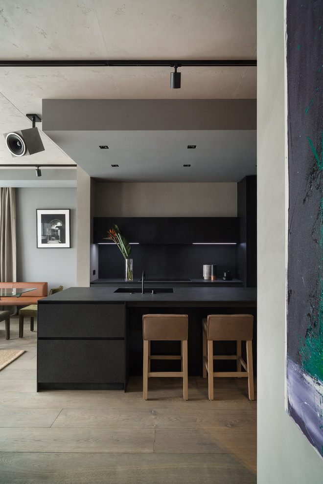 Photo of a mid-sized contemporary l-shaped open plan kitchen in Moscow with an integrated sink, flat-panel cabinets, black cabinets, granite benchtops, black splashback, stone slab splashback, black appliances, concrete floors, with island, blue floor and black benchtop.