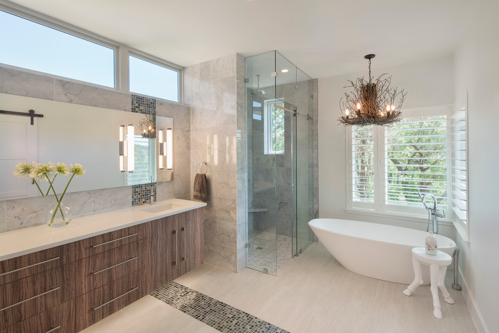 This is an example of a contemporary master bathroom in Austin with flat-panel cabinets, medium wood cabinets, a freestanding tub, a corner shower, gray tile, multi-coloured tile, mosaic tile, white walls, an undermount sink and a sliding shower screen.