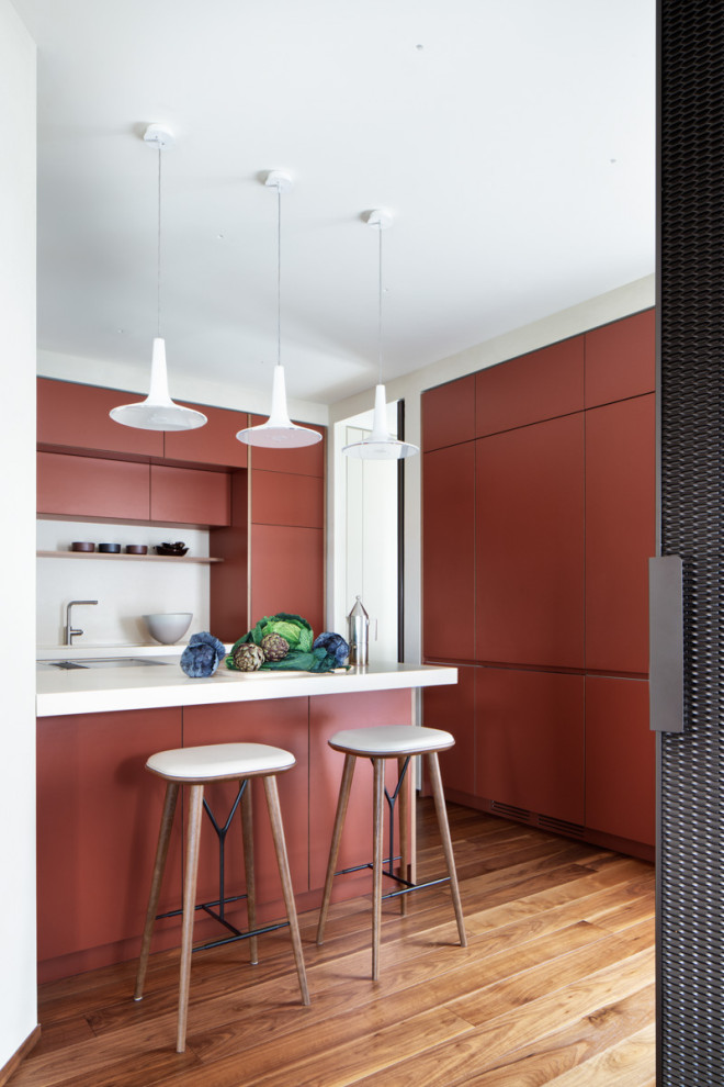 Inspiration for a contemporary l-shaped kitchen in Milan with flat-panel cabinets, red cabinets, white splashback, panelled appliances, medium hardwood floors, a peninsula, brown floor and white benchtop.