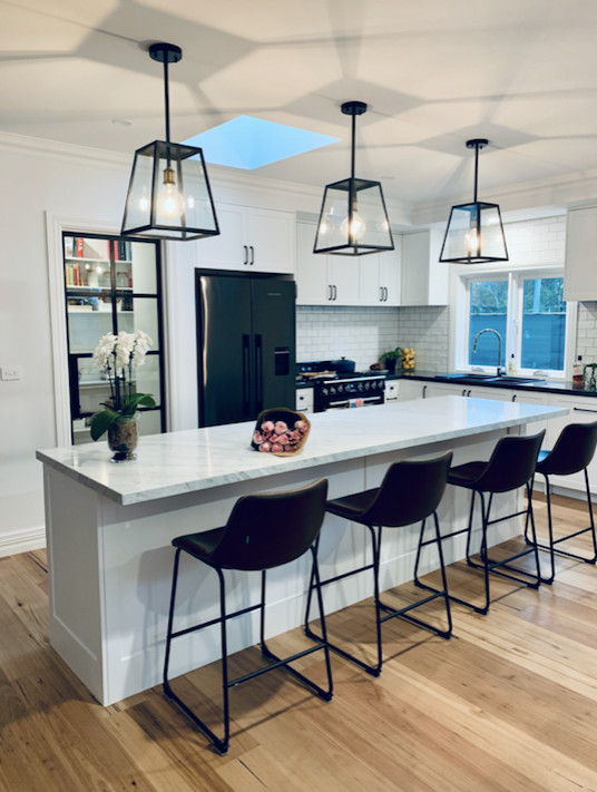 Mid-sized transitional l-shaped kitchen pantry in Melbourne with a double-bowl sink, shaker cabinets, white cabinets, marble benchtops, white splashback, subway tile splashback, black appliances, light hardwood floors, with island, beige floor and grey benchtop.