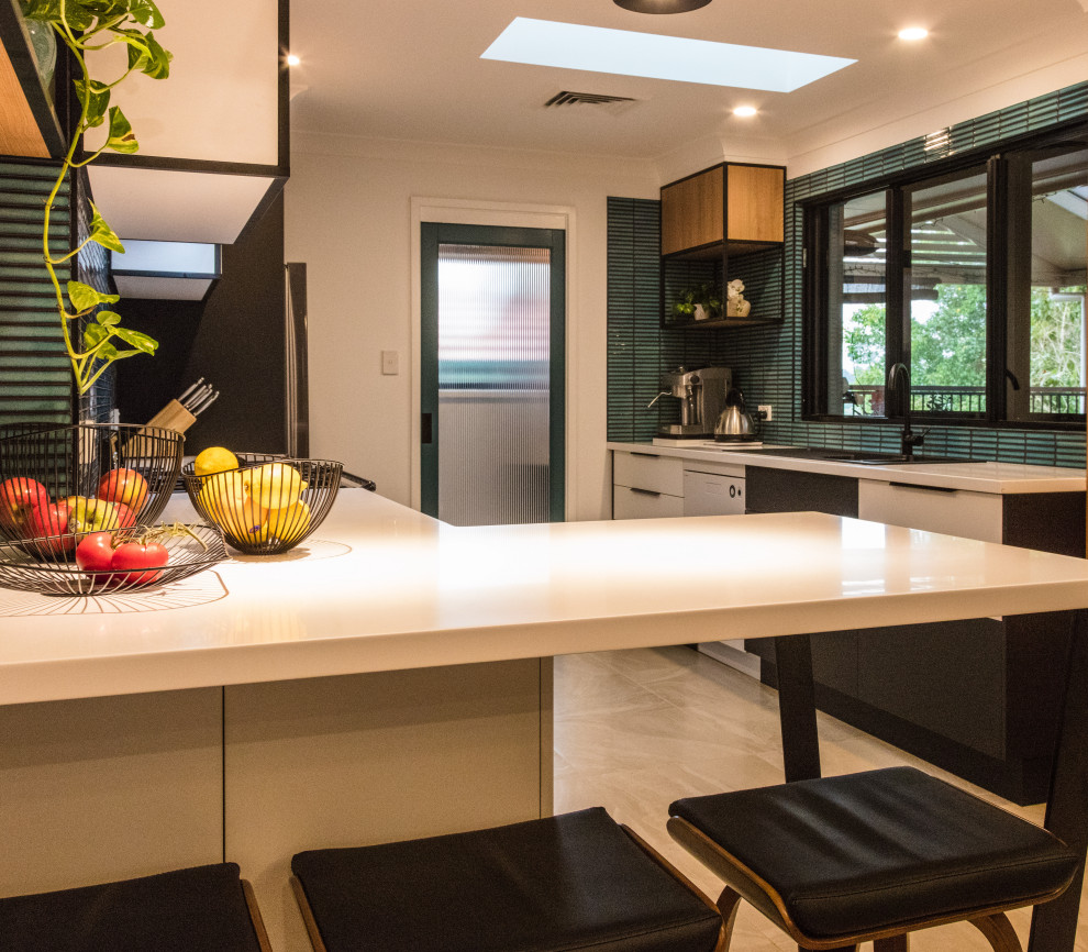 Inspiration for a mid-sized midcentury galley eat-in kitchen in Sydney with a drop-in sink, flat-panel cabinets, white cabinets, solid surface benchtops, green splashback, mosaic tile splashback, black appliances, ceramic floors, no island, beige floor and white benchtop.