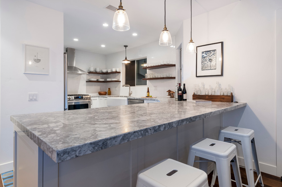 Inspiration for a beach style u-shaped kitchen in San Diego with a farmhouse sink, white cabinets, granite benchtops, white splashback, ceramic splashback, stainless steel appliances and concrete floors.