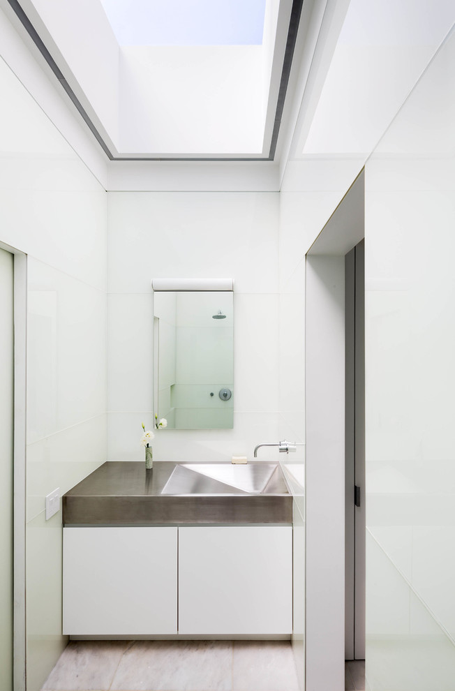 Modern bathroom in New York with an integrated sink, flat-panel cabinets, white cabinets, stainless steel benchtops, white walls and marble floors.