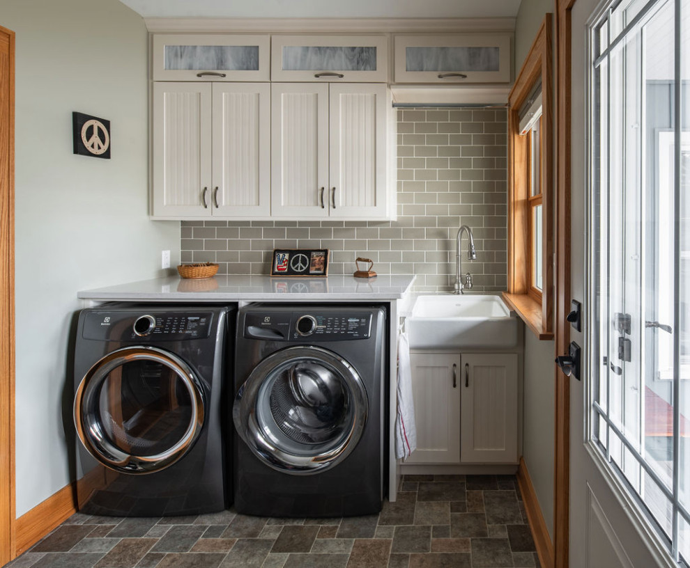 Photo of a mid-sized traditional single-wall dedicated laundry room in Columbus with a farmhouse sink, recessed-panel cabinets, white cabinets, quartz benchtops, green walls, vinyl floors, a side-by-side washer and dryer, multi-coloured floor and white benchtop.