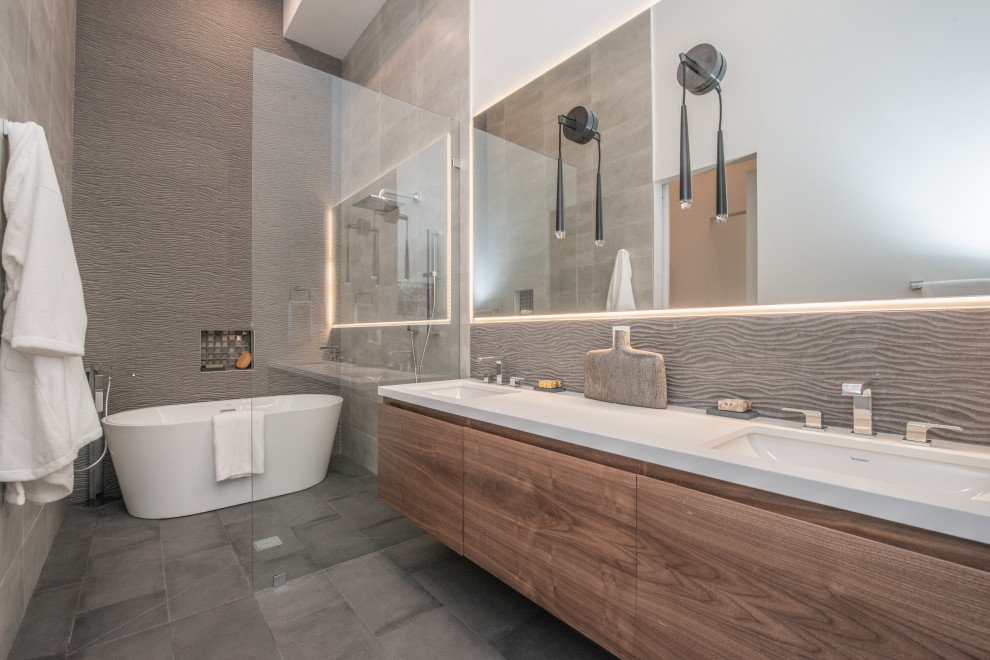 Inspiration for a large contemporary ensuite bathroom in Los Angeles with flat-panel cabinets, medium wood cabinets, a freestanding bath, a built-in shower, white walls, a submerged sink, engineered stone worktops, grey floors, white worktops, double sinks, a floating vanity unit, a wall mounted toilet, grey tiles, porcelain tiles, porcelain flooring, a hinged door and a wall niche.