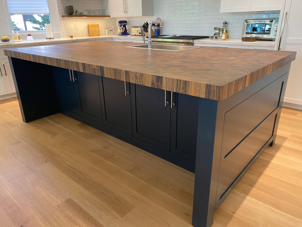This is an example of a large contemporary l-shaped eat-in kitchen in Boston with a drop-in sink, recessed-panel cabinets, wood benchtops, white splashback, stainless steel appliances, light hardwood floors, with island, brown floor and multi-coloured benchtop.