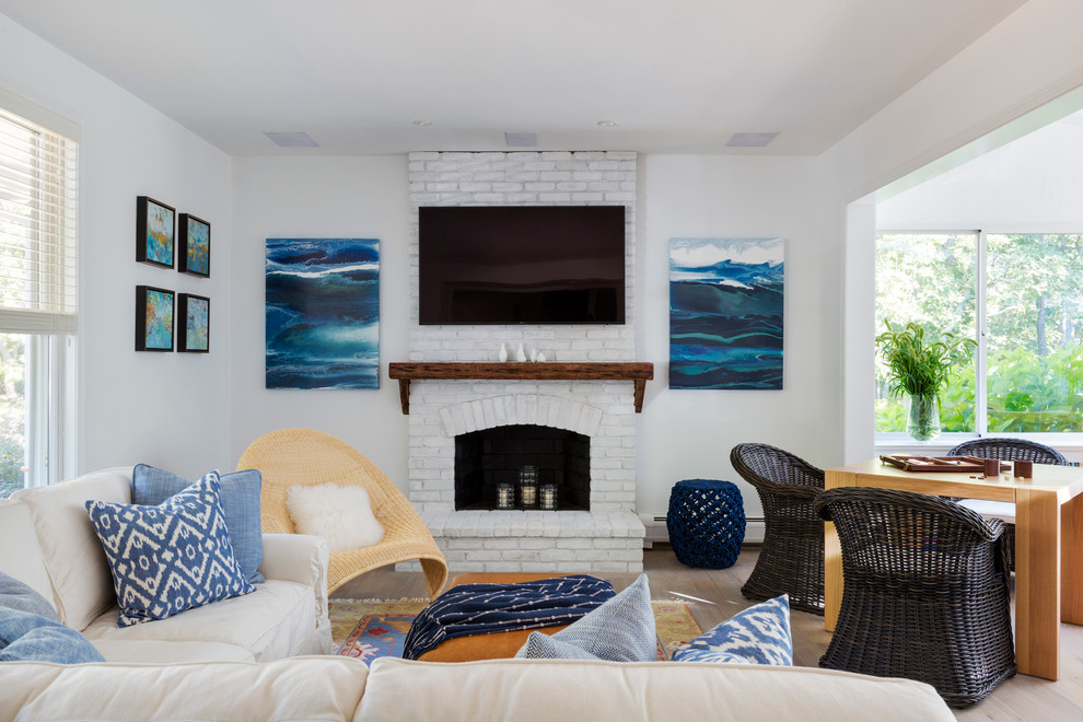 This is an example of a mid-sized beach style open concept family room in Boston with a game room, white walls, light hardwood floors, a standard fireplace, a brick fireplace surround and a wall-mounted tv.