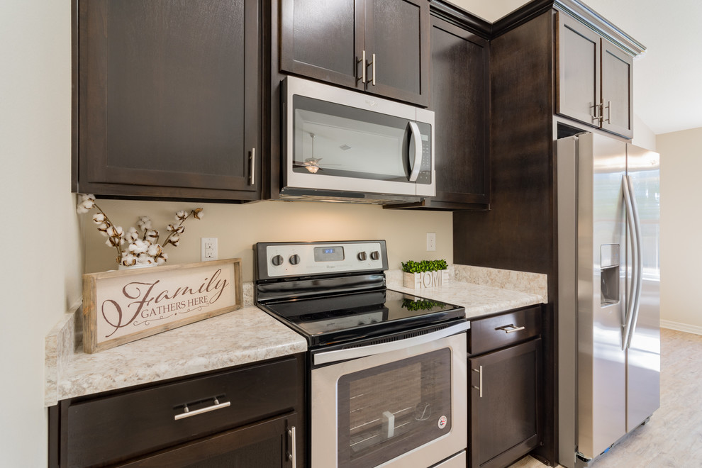 Mid-sized arts and crafts vinyl floor and gray floor eat-in kitchen photo with recessed-panel cabinets, dark wood cabinets, laminate countertops, stainless steel appliances and an island