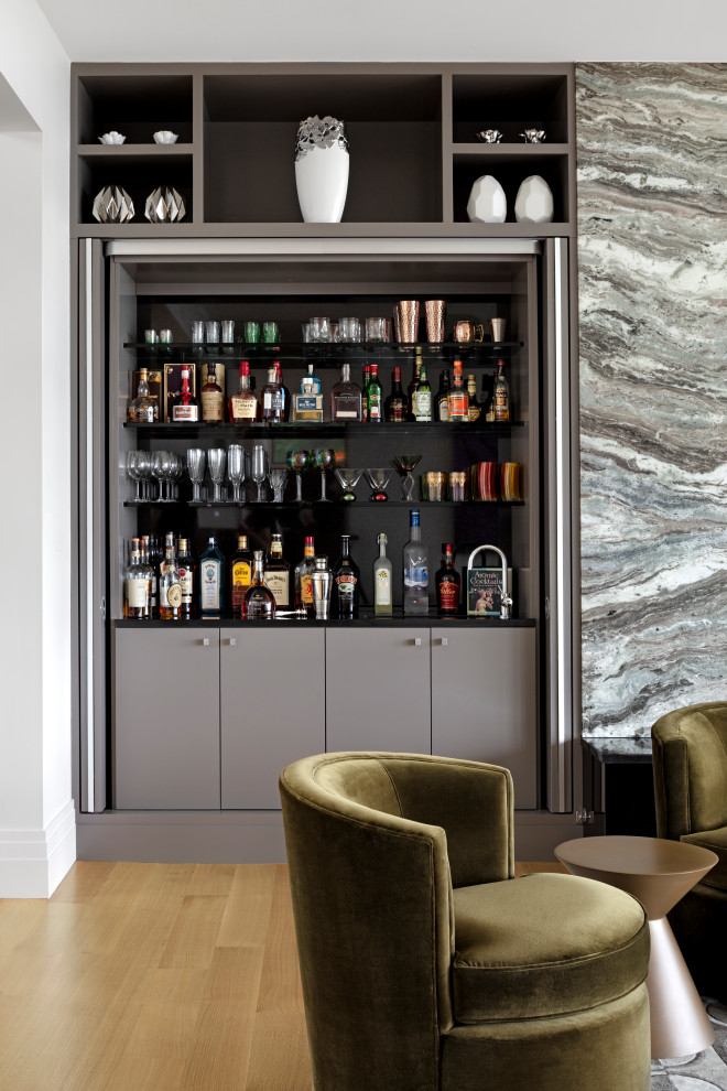 Mid-sized contemporary single-wall wet bar in Baltimore with an integrated sink, grey cabinets, grey splashback, light hardwood floors, brown floor and black benchtop.