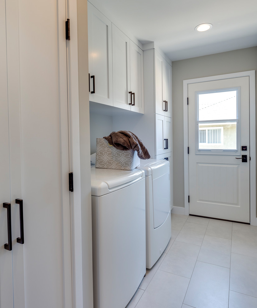 Mid-sized transitional single-wall dedicated laundry room in Los Angeles with shaker cabinets, white cabinets, grey walls, porcelain floors, a side-by-side washer and dryer and white floor.