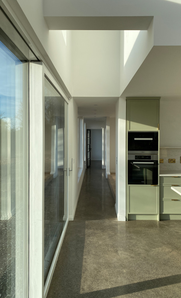 Bild på en stor funkis beige parallell beige liten tvättstuga, med luckor med upphöjd panel, beige skåp, granitbänkskiva, betonggolv och grått golv