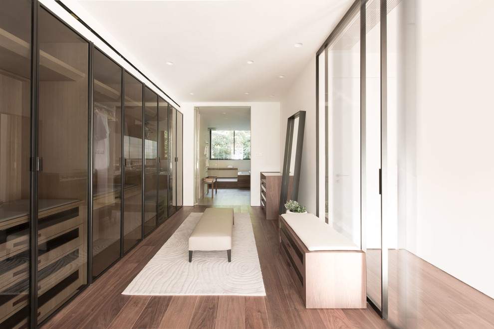 This is an example of a mid-sized contemporary gender-neutral walk-in wardrobe in Hong Kong with glass-front cabinets, dark hardwood floors and medium wood cabinets.